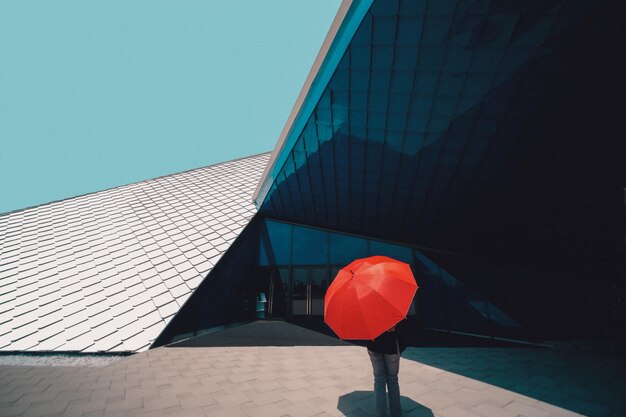 Photo personne avec un parapluie debout par le bâtiment contre le ciel clair