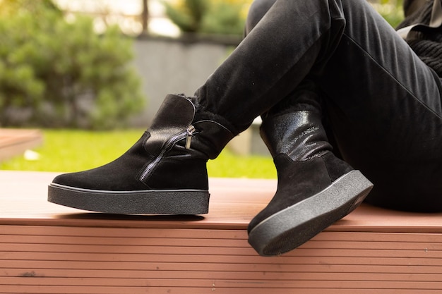 Une personne portant des bottes noires est assise sur un banc devant un fond d'herbe verte.