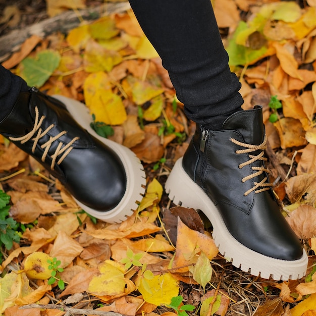 Une personne portant des bottes noires et un pantalon noir se tient debout dans les feuilles.