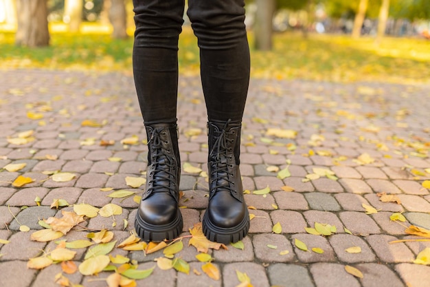 Une personne portant des bottes noires se tient sur une passerelle en brique dans les feuilles d'automne.