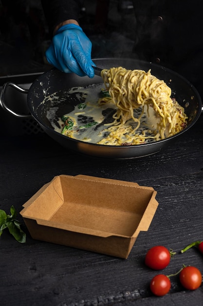 Une personne portant un gant bleu ajoute des pâtes dans une casserole.