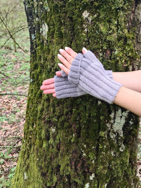 Une personne portant un gant gris est appuyée contre un tronc d'arbre.