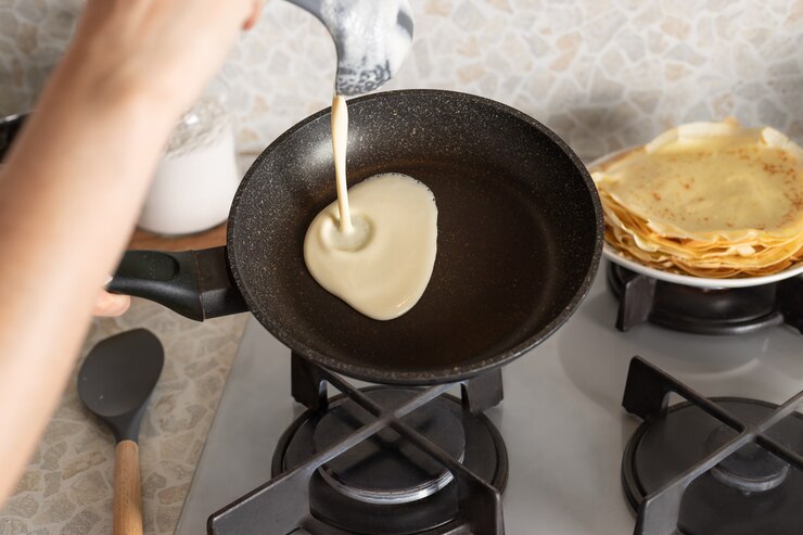 Personne qui cuisine des crêpes minces sur une poêle à frire dans la cuisine