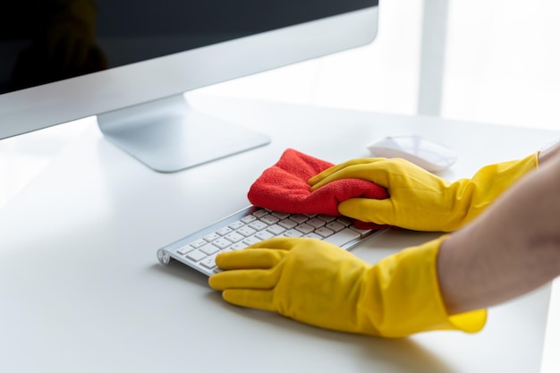 La personne qui nettoie la salle de nettoyage utilise un chiffon pour essuyer le clavier de l'ordinateur dans le bureau de l'entreprise Personnel de nettoyage Concept de propreté dans l'organisation