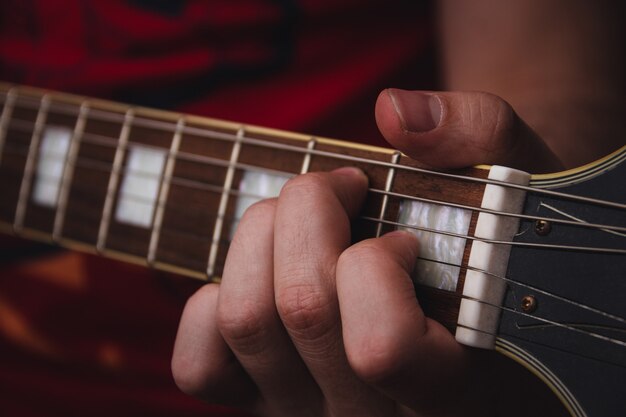 Personne qui pince les cordes sur les frettes d'une guitare électrique. Mise au point sélective. Espace de copie.