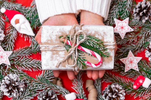 Une personne reçoit un cadeau de Noël sur fond de branches de sapin et d'ornements.