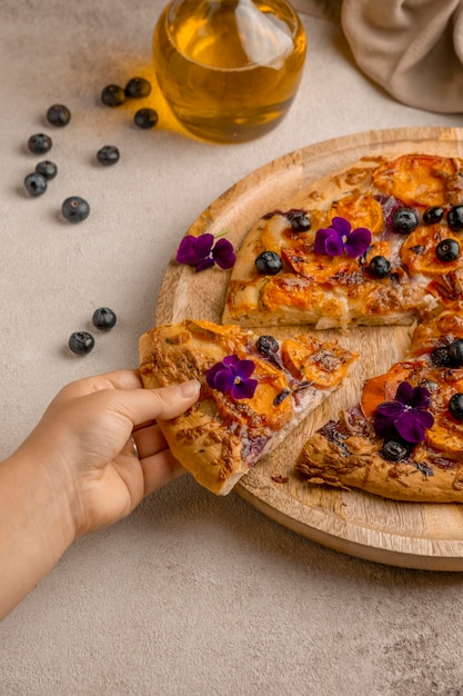 Photo personne saisissant une délicieuse tranche de pizza aux myrtilles et pétales de fleurs