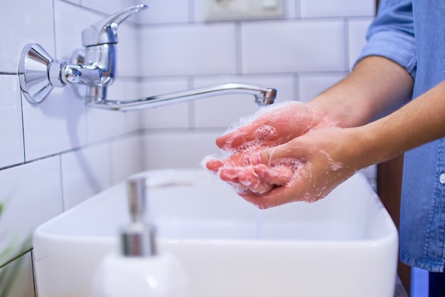 La personne se lave les mains dans le lavabo de la salle de bain avec du savon antibactérien liquide. Protection et prévention quotidiennes contre les virus, les microbes et les bactéries