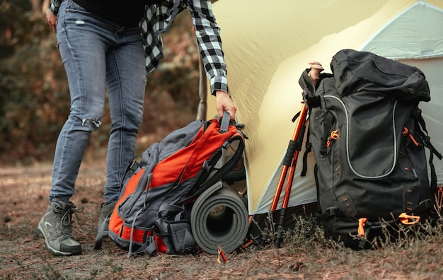 Personne se préparant à faire de la randonnée et mettant sur le sol des sacs à dos et des tapis de kare près de la tente en camping pla...