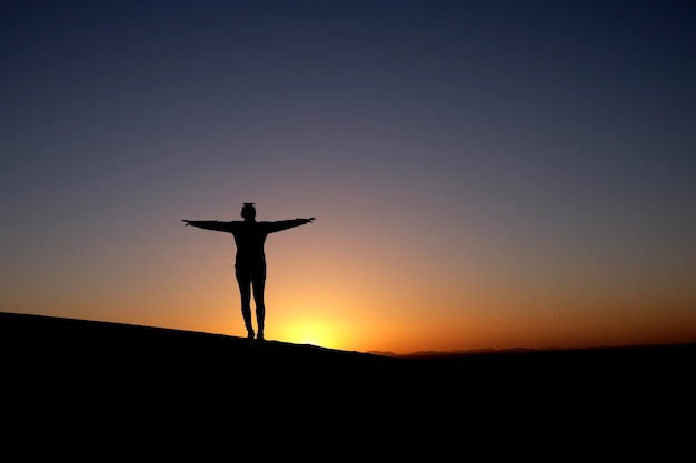 Photo une personne se tient les bras tendus devant un coucher de soleil.