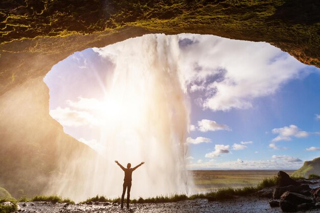 Photo une personne se tient devant une chute d'eau avec le soleil qui brille au fond.