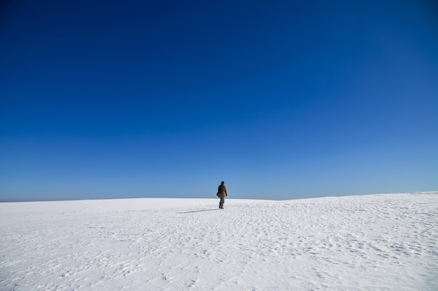 Personne seule marchant dans un pays couvert de neige sous un ciel lumineux