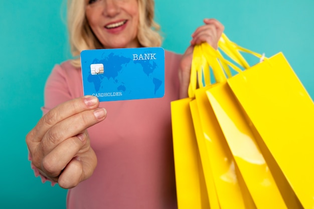 Personne de sexe féminin sur le mur bleu tenant une carte de crédit et de nombreux sacs à provisions jaunes.