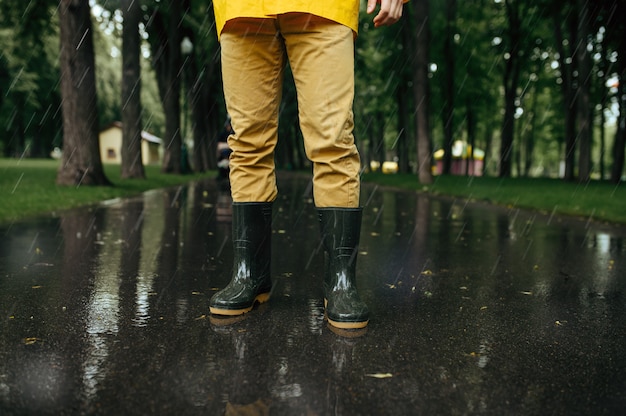 Personne de sexe masculin en cape de pluie et bottes en caoutchouc, temps humide dans la ruelle. L'homme pose dans le parc d'été en jour de pluie. Protection contre l'eau, gouttes