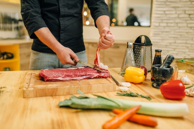 Personne de sexe masculin avec couteau coupe la viande crue sur planche de bois