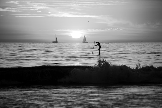 Photo personne stand up paddle au crépuscule sur une mer avec de belles couleurs de coucher de soleil