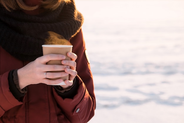 Personne avec une tasse de café chaud à l'extérieur au coucher du soleil