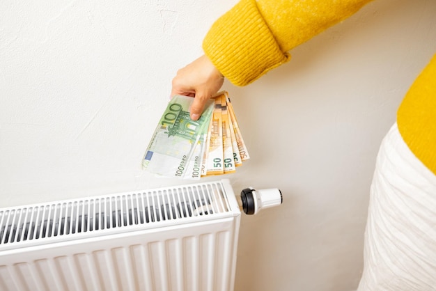 Personne tenant des billets en euros près d'un radiateur à la maison