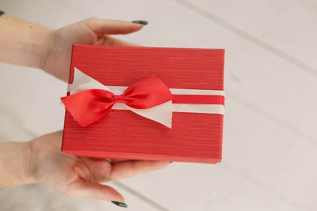 Une personne tenant une boîte cadeau rouge avec un arc rouge.
