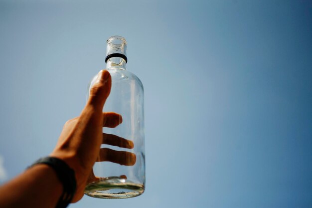 Photo personne tenant une bouteille de verre contre un ciel bleu clair