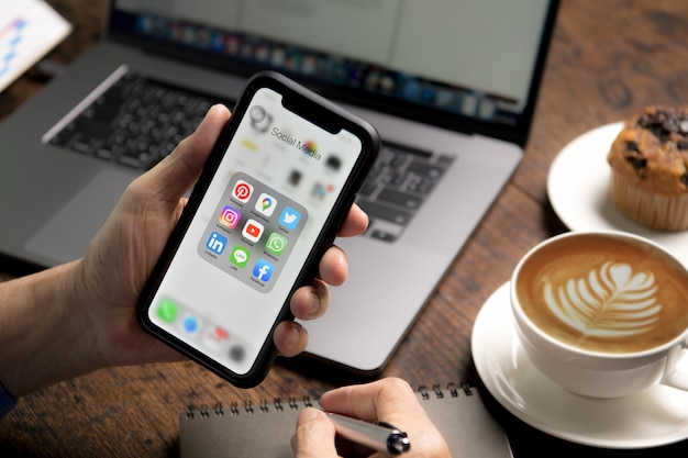 Personne tenant un smartphone avec des icônes de médias sociaux sur l'écran du café