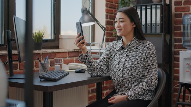 Personne tenant un smartphone pour parler en appel vidéo à un collègue dans le bureau de démarrage. Femme d'affaires utilisant une conférence à distance en ligne sur un téléphone portable pour discuter de la planification de projet. Conférence vidéo