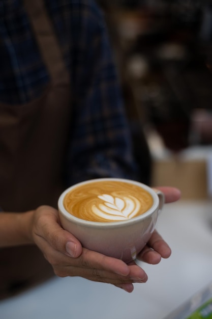 Une personne tenant une tasse de café avec un dessin d'art latte dessus