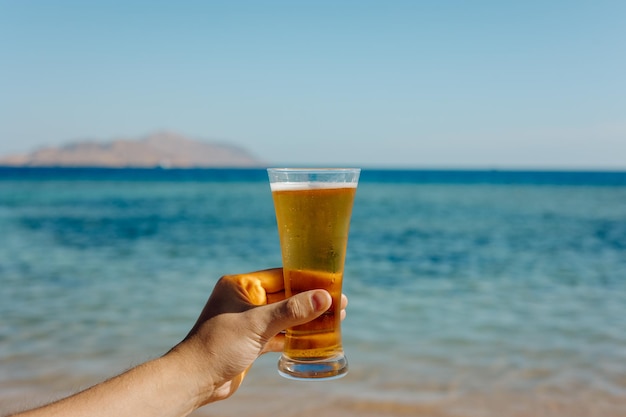 La personne tenant un verre de bière sur fond de mer