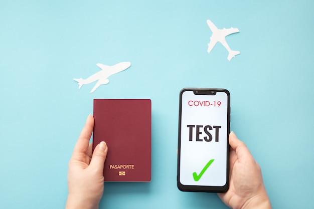 personne titulaire d'un passeport et d'un smartphone avec un test covid sur fond bleu avec des avions