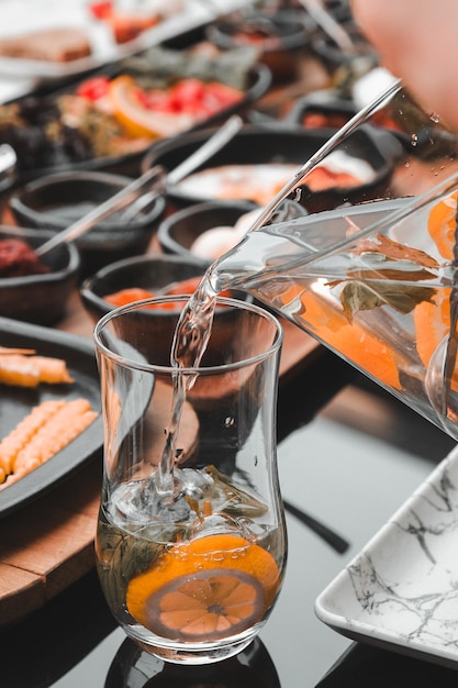 une personne versant de l'eau dans un verre avec des oranges et une cuillère