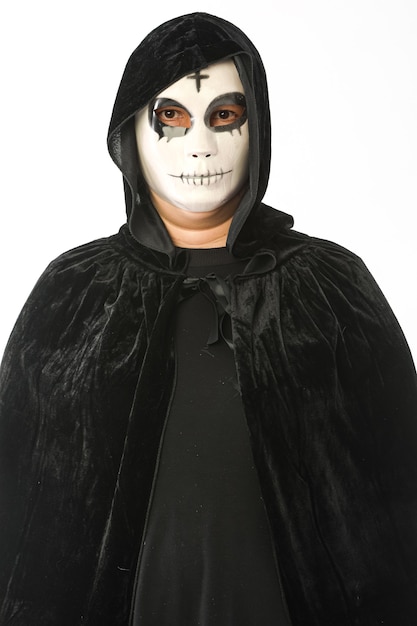 Personne vêtue d'un masque blanc avec croix sur le front et cape de velours noir avec capuche, sur fond blanc. Concept de carnaval, Halloween et jour des morts.