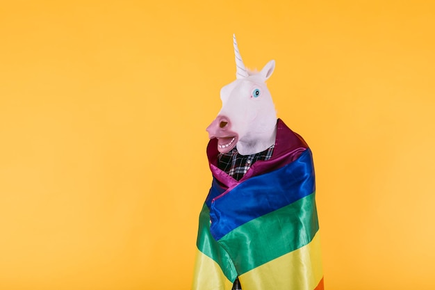 Photo personne vêtue d'un masque de licorne avec une chemise à carreaux tenant un drapeau lgtbq arc-en-ciel sur fond jaune concept de transsexualité gay pride et de droits lgtbq