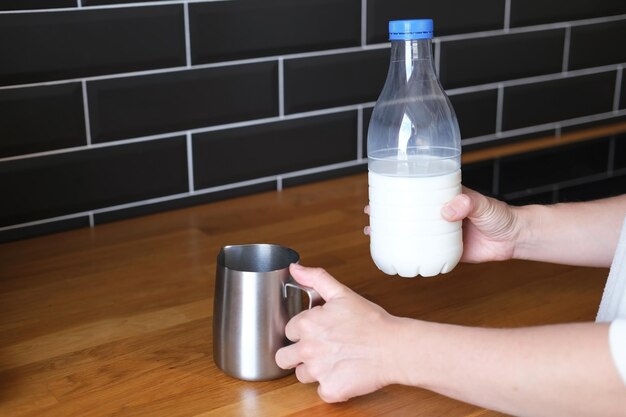 Une personne veut verser du lait dans un pichet à lait pour faire du cappuccino du matin à la maison