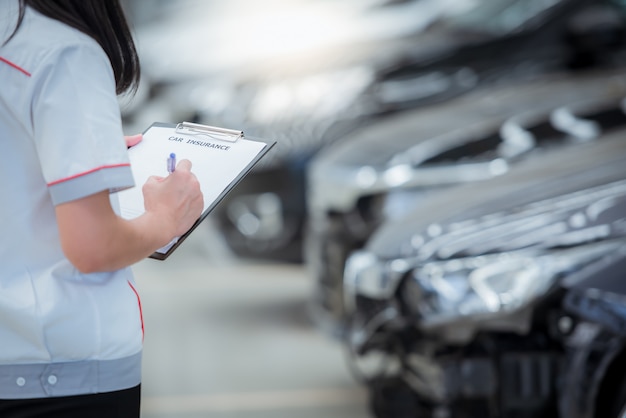 Le personnel de l'agent d'assurance écrit sur le presse-papiers tout en vérifiant la voiture après avoir été évalué et a procédé à la réclamation de l'accident - la voiture a une assurance contre les accidents.