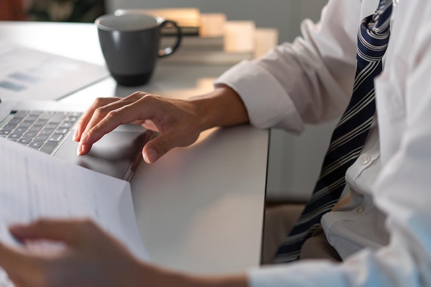 personnel de bureau en cravate lâche assis à son bureau lisant un document et tapant sur le cahier