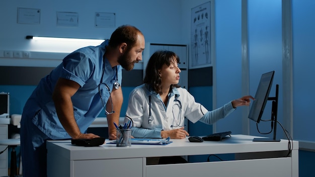 Personnel clinique regardant un écran d'ordinateur analysant l'expertise médicale du patient tout en discutant d'un traitement médicamenteux pour aider à guérir la maladie. Médecin et infirmière travaillant de nuit au bureau de l'hôpital