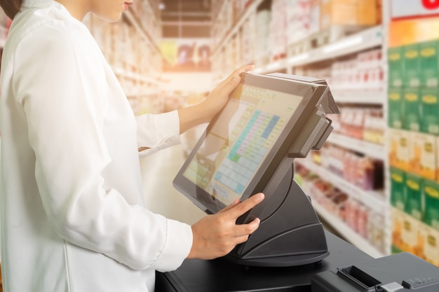 Le personnel féminin de caissier permanent et travaillant avec POS ou machine de point de vente au comptoir du supermarché.