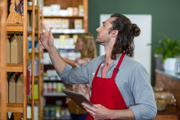 Personnel masculin tenant une tablette numérique et vérifier les produits d'épicerie sur l'étagère
