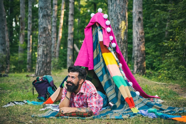 Personnes actives Bel homme barbu à l'intérieur de la tente de camping Tente de jeu confortable pour homme Cabane de branches Camping de repos