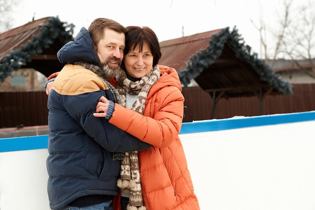 Personnes d'âge moyen heureux couple homme et femme visitant une patinoire en plein air en hiver câlins sourires