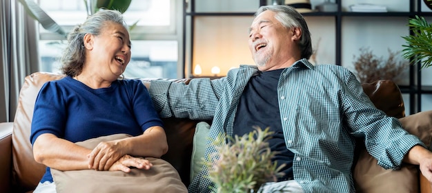 Les personnes âgées asiatiques âgées à la retraite épousent le style de vie de bien-être ciuple ensemble chez les personnes âgées rient sourire ensemble avec amour et liaison sur le canapé dans le fond intérieur de la maison de salon