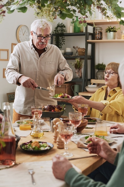 Personnes âgées assises à la table à manger et mangeant de la nourriture lors d'une réunion à la maison