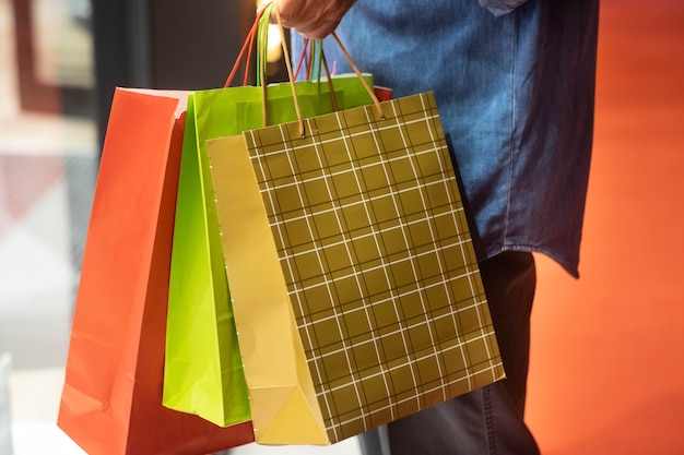 Personnes âgées avec une chemise en jean faisant du shopping en soirée tout en profitant d'offres et de réductions. Sur son bras beaucoup de sacs à provisions