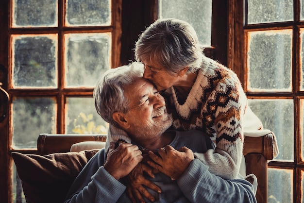 Les personnes âgées à la maison aiment s'embrasser et se soucier les unes des autres. Bonne relation homme mûr et femme ensemble. Vieil homme assis sur le canapé et femme âgée l'embrassant avec soin