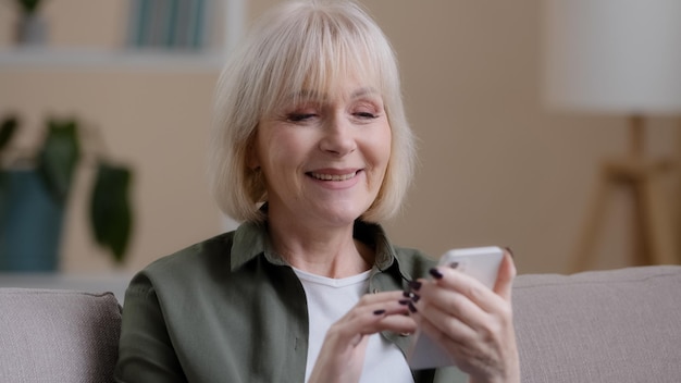 Personnes âgées matures matures 60s caucasian woman with phone female smiling utilise l'application mobile à la maison achète