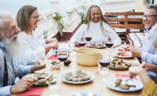 Personnes âgées multiraciales s'amusant dans le dîner au patio