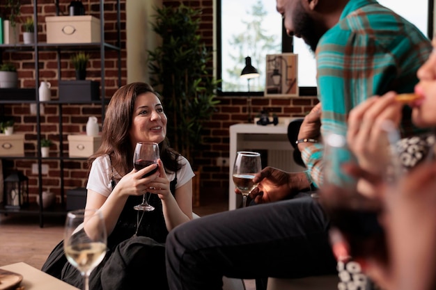 Des personnes amicales et diverses célébrant leur anniversaire tout en buvant des boissons alcoolisées ensemble à la maison. Groupe multiethnique d'amis proches assis dans le salon tout en faisant la fête du vin.