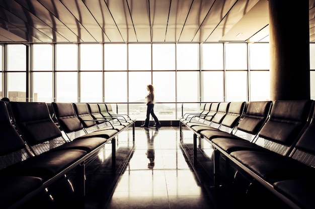 Personnes attendant de voyager et de voler à l'aéroport - femme marchant nerveuse à l'intérieur de la zone des portes vides près de la grande fenêtre avec vue sur les avions - concept de retard au départ ou à l'arrivée