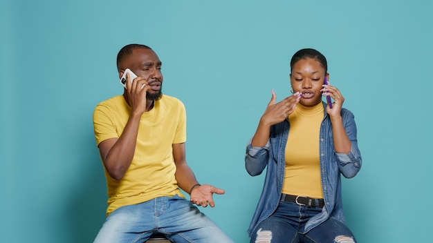 Personnes ayant une conversation téléphonique pendant qu'elles sont assises ensemble en studio. Homme et femme utilisant une connexion Internet pour parler sur la communication par téléphone mobile. Couple moderne avec smartphone