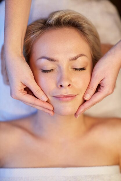 Personnes, beauté, spa, mode de vie sain et concept de relaxation - gros plan de la belle jeune femme allongée avec les yeux fermés et ayant un massage du visage ou de la tête au spa